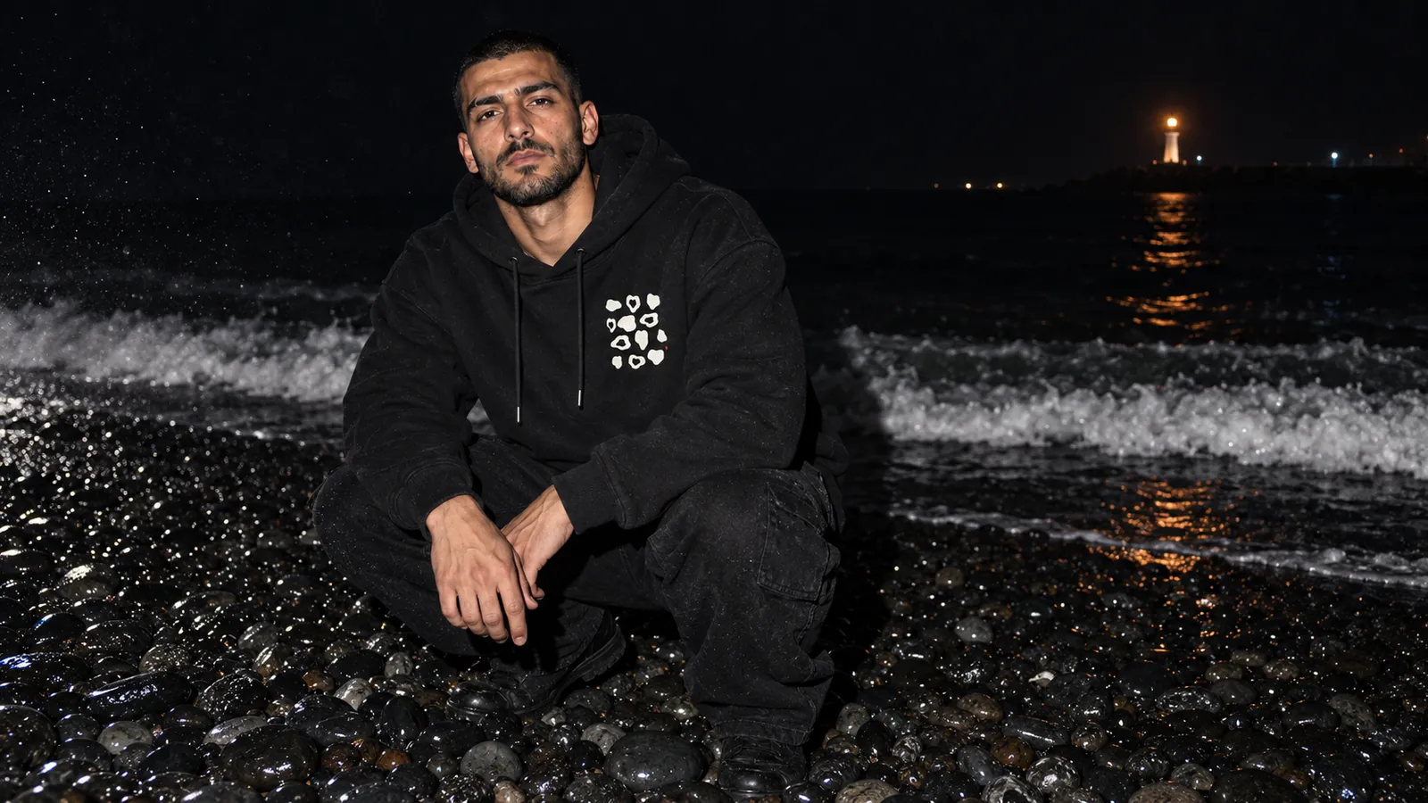 Çakıltaşı desenli siyah hoodie giyen bir model, gece siyah çakıllı bir sahilde