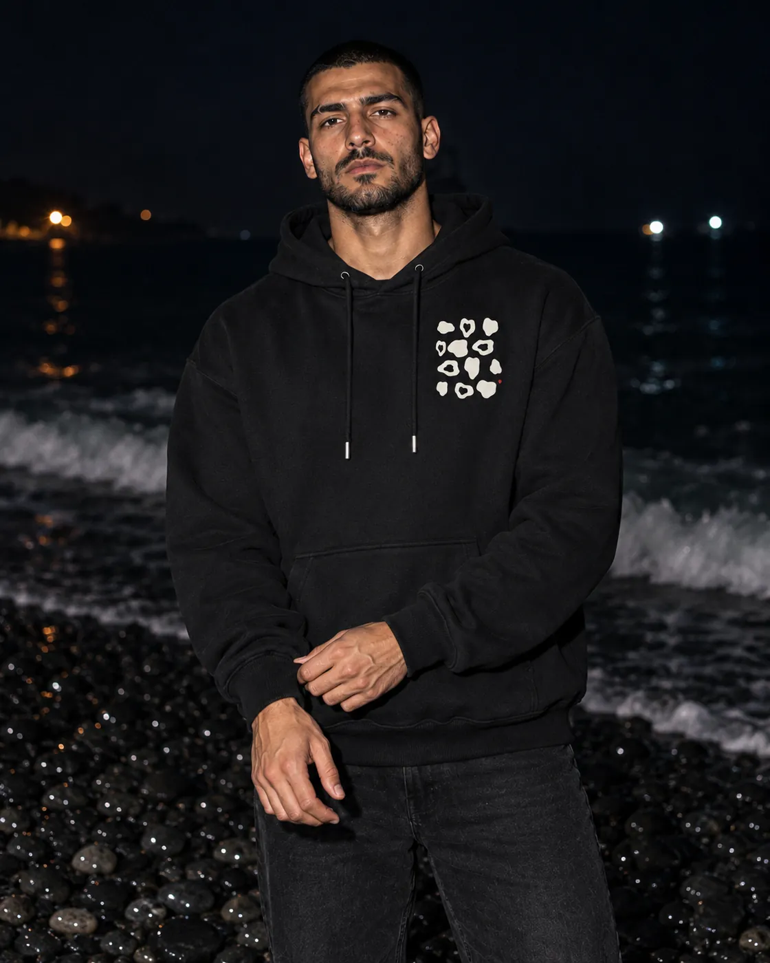 Çakıltaşı Premium Siyah Hoodie: model üzerinde, gece siyah çakıllı bir sahilde