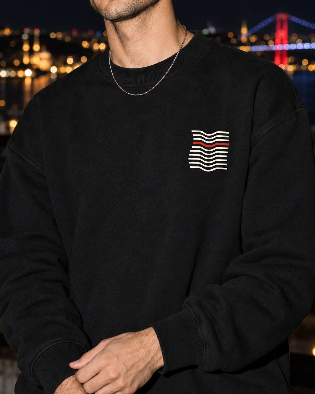 Kıvrım Premium Siyah Sweatshirt: göğüsteki baskı yakından, gece Boğaz'a bakan bir çatıda