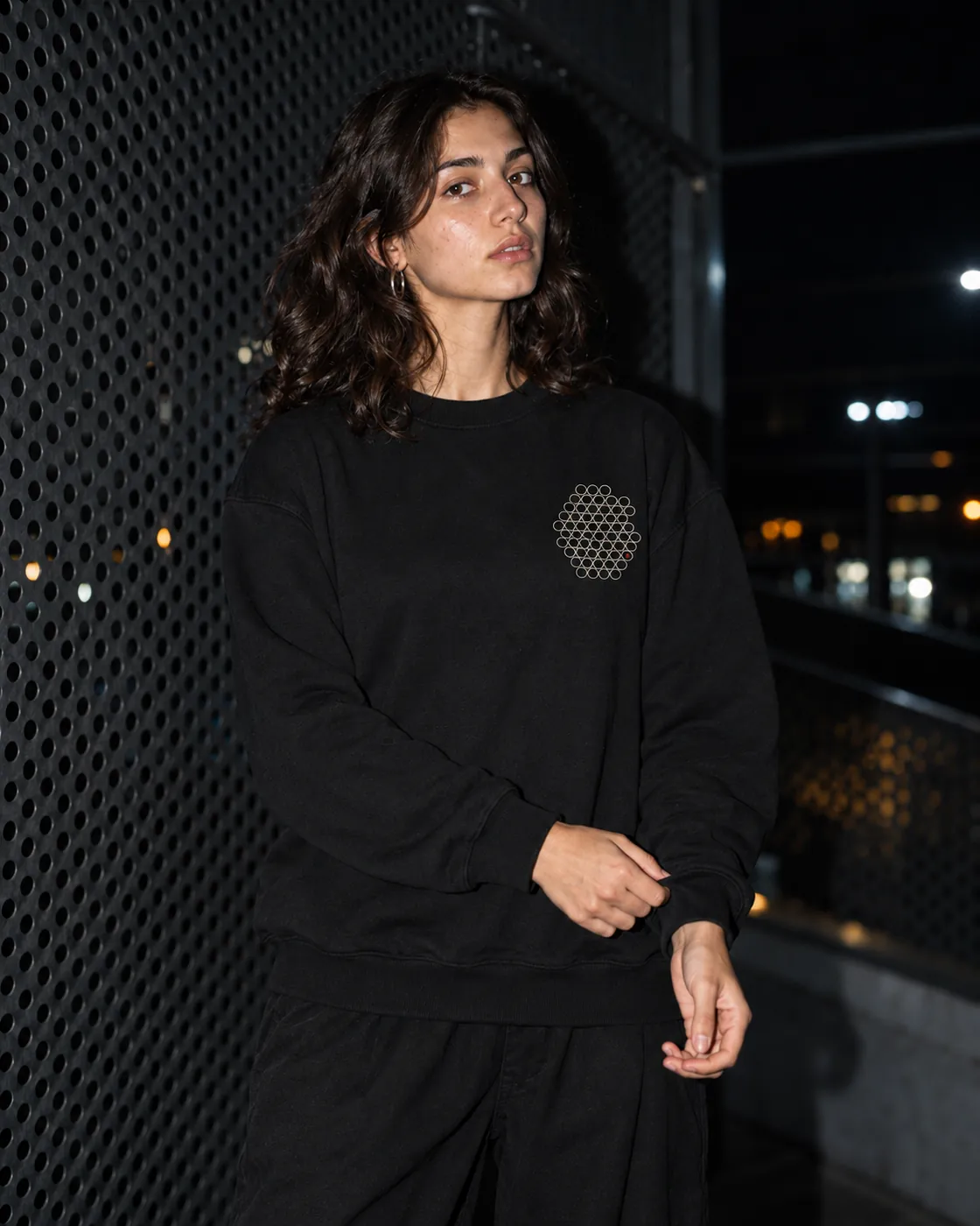 Gözenek Premium Siyah Sweatshirt: model üzerinde, gece delikli metal bir cephenin önünde